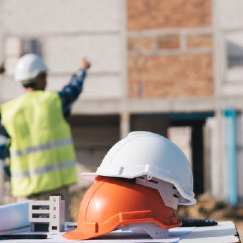 Structural engineer and architect working with blueprints discuss at the outdoors construction site.